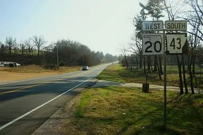 A rural road with cars, trees, and road signs for Highway 20 West and Highway 43 South.