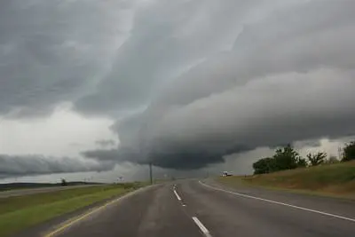 A dark, ominous storm cloud looms over an empty, curving highway in a rural landscape.
