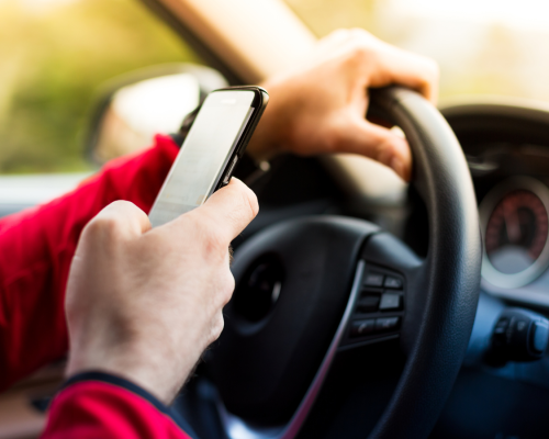 A driver wearing a red jacket uses a smartphone while driving, illustrating distracted driving behavior and the risks associated with texting and driving in Oklahoma City.