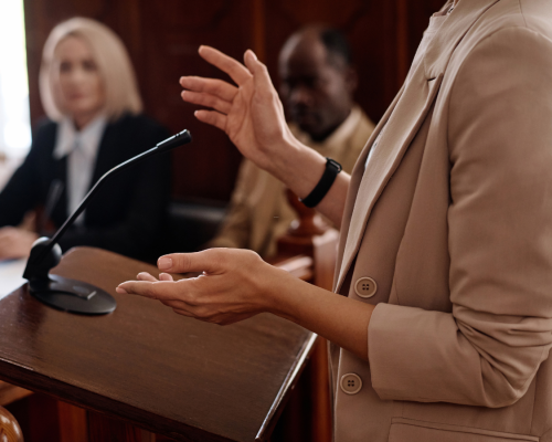 An attorney stands and speaks at a courtroom podium with a microphone, gesturing while addressing the court, symbolizing the role of expert witnesses in Oklahoma City car accident trials.