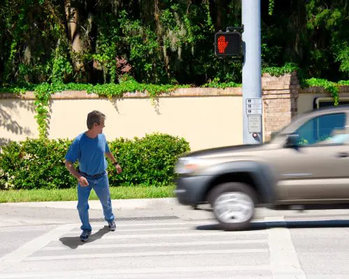 A man is jaywalking across an intersection when the signal is clearly showing the do not cross symbol.