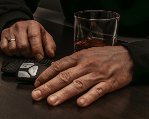 Close-up of a person’s hands resting near a car key fob and a glass of alcohol on a table, symbolizing impaired driving and the serious consequences that can lead to fatal DUI accidents and wrongful death claims in Oklahoma City.