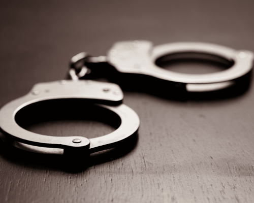 Close-up of metal handcuffs resting on a wooden surface, symbolizing the criminal justice system and contrasting with civil personal injury claims in Oklahoma.