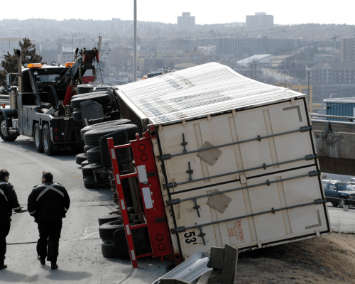 Overturned semi-truck lying on its side along a roadway with a tow truck and responders nearby, illustrating the serious consequences of truck driver errors and rollover accidents in Oklahoma City.