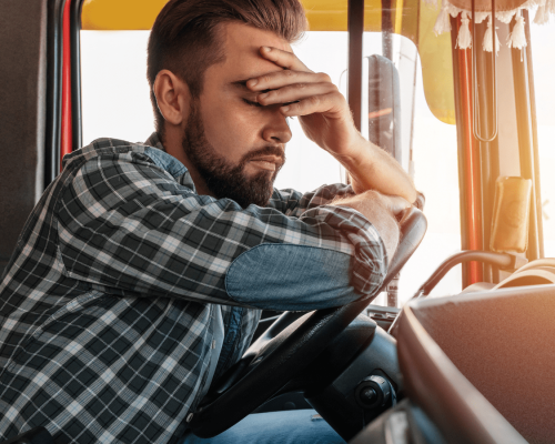 Fatigued truck driver sitting behind the wheel with eyes closed and hand on his forehead, illustrating the dangers of driver exhaustion and its role in serious truck accidents in Oklahoma City.