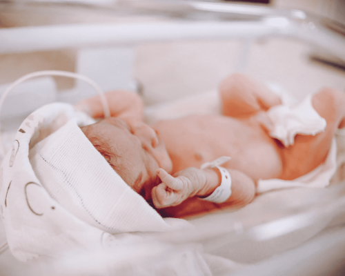 Newborn baby lying in a hospital bassinet wearing a medical cap and identification band, representing the critical care environment where preventable birth injuries can occur and lead to legal claims in Oklahoma City.