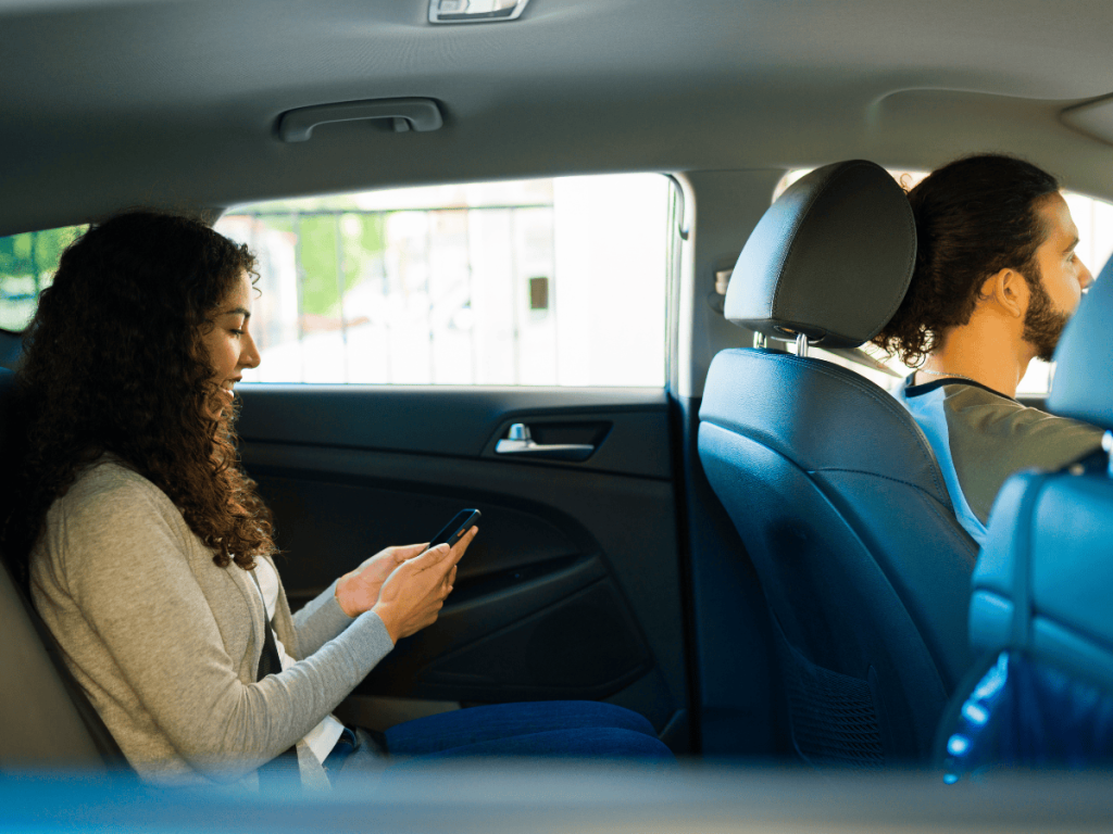 Passenger seated in the back of a rideshare vehicle looks at her phone while the driver operates the car, illustrating a typical rideshare setting and the risks passengers may face in Oklahoma City accidents.