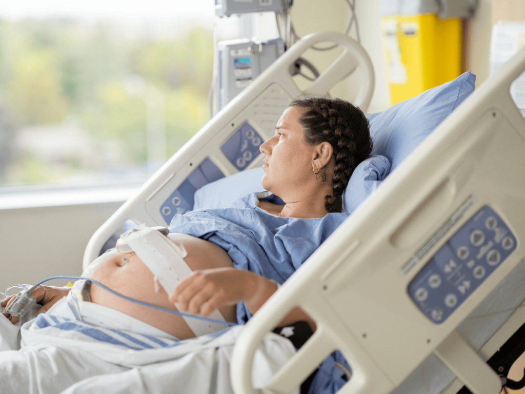 Pregnant patient in a hospital bed with fetal monitoring equipment, illustrating labor and delivery care, birth injuries, and potential medical malpractice involving assisted delivery tools.